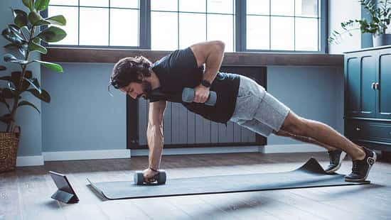 Mann macht einseitige Plank mit Hanteltraining im Home-Gym.