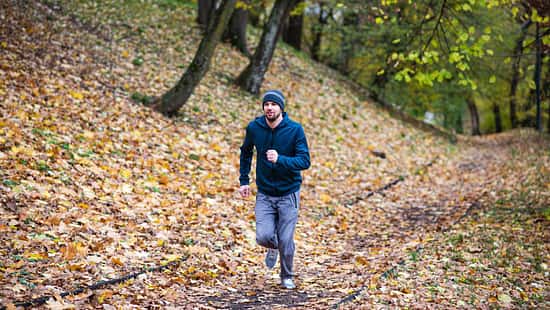 Mann läuft im Wald, umgeben von Herbstlaub
