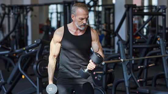 Älterer Mann trainiert mit Kurzhanteln im Fitnessstudio und macht Bizepscurls.