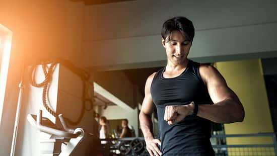 Sportlicher Mann im Fitnessstudio schaut auf seine Smartwatch.