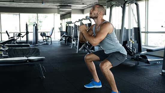 Junger Mann im Fitnessstudio führt Squats aus.