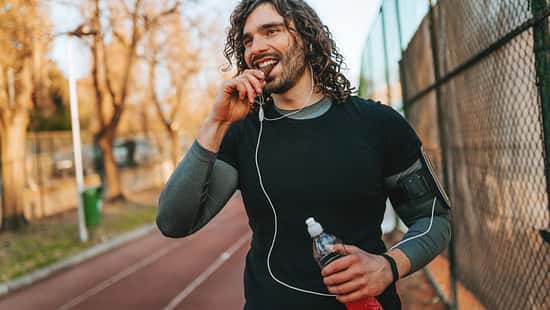 Mann in Sportkleidung geht draußen auf einer Laufstrecke und isst einen Proteinriegel