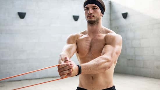 Ein Mann trainiert oberkörperfrei in einem Raum und hält mit beiden Armen ein Stretching-Band