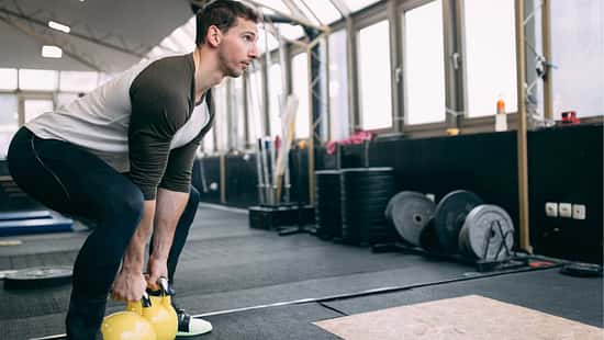 Mann führt in einem Fitnessstudio eine Squatbewegung mit Kettleballs aus