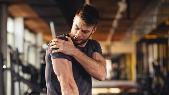 Handsome young man feeling the pain in shoulder at the gym