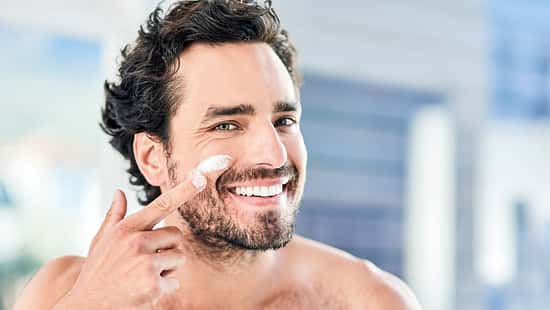Ein Mann trägt lächelnd Sonnencreme im Gesicht auf
