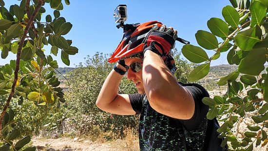 Mann in mediterraner Landschaft setzt sich einen Fahrradhelm mit einer daran befestigter Actionkamera auf