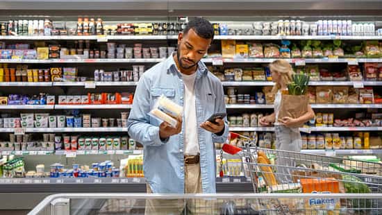 Mann steht im Supermarkt vor dem Kühlregal und schaut prüfend auf die Rückseite eines Produktes
