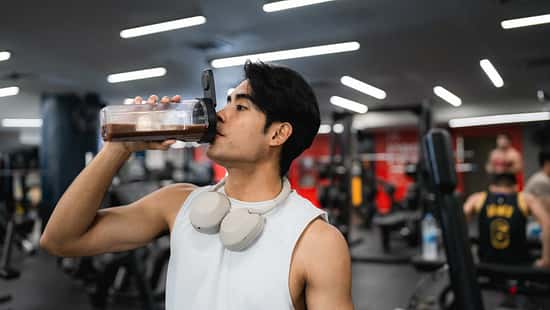 Ein junger Mann sitzt im Fitnessstudio und trinkt einen Proteinshake.