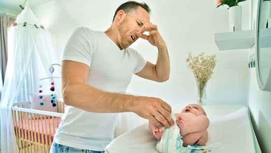 Vater wickelt sein Baby und hält sich die Nase zu