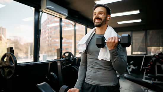 Junger Sportler, der mit Kurzhanteln im Fitnessstudio trainiert
