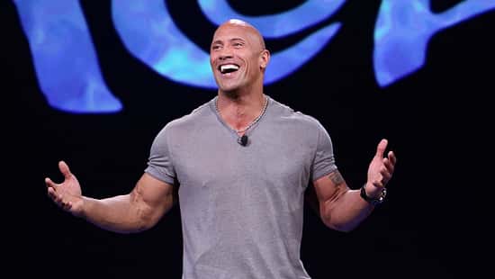 Dwayne Johnson im blaugrauen Shirt mit ausgebreiteten Armen, der auf der Premiere von "Moana" in die Kamera lacht
