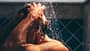 GettyImages.de/Mariia Siurtukova Engrossed in his grooming ritual, a man rinses his hair, the water's embrace enhancing the meditative quality of his daily routine.