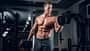 Muscular shirtless male doing biceps exercise with dumbbells.