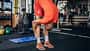 Ein junger Mann in orangener Sportkleidung dehnt sich vor dem Training im Fitnessstudio.