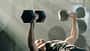 Mann trainiert im Fitnessstudio mit Hanteln und liegt auf der Hantelbank Mann trainiert im Fitnessstudio mit Hanteln und liegt auf der Hantelbank