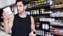 Ein Mann steht vor einem Regal mit Protein-Supplementen und schaut sich die Inhaltsstoffe von zwei Produkten an