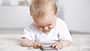 Ein Baby liegt auf dem Fußboden und spielt an einem Smartphone