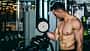 Ein trainierter Mann steht oberkörperfrei im Gym und beobachtet seinen großen Bizeps, während er ihn mit Kurzhanteln trainiert Ein trainierter Mann steht oberkörperfrei im Gym und beobachtet seinen großen Bizeps, während er ihn mit Kurzhanteln trainiert