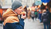 Mann mit Mütze isst auf dem Weihnachtsmarkt eine süße gefüllte Blätterteigrolle