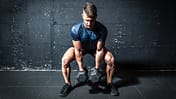 Mann hält im Squat zwei schwere Kurzhanteln und ist im Begriff, sie hochzustemmen