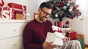 Smiling,Young,Man,Opening,Christmas,Gift,At,Home