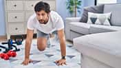Mann macht im Wohnzimmer Fitnessübungen.