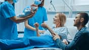 Im Kreisssaal: Eine Mutter bekommt ihr neugeborenes Kind in die Arme gelegt, der Vater sitzt daneben