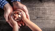 Kinderhände übergeben ein Glas mit Kleingeld an erwachsene Hände