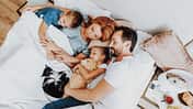 Vater, Mutter, zwei Kinder und eine Katze liegen alle zusammen in einem großen Bett und schlafen zufrieden