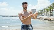 handsome,sunscreen,young,exterior,skin,tourism,guy,lotion,protection,bottle,shirtless,body,naked,sun,sea,summer,tourist,holidays,swimwear,casual,hispanic,vacation,swimsuit,man,sunny,applying,expression,beard,nature,health,cream,portrait,water,lifestyle,outdoor,standing,sunlight,ocean,outdoors,promenade,seaside,person,beach,adult,travel,male,care,fashion Young,Hispanic,Man,Tourist,Wearing,Swimsuit,Applying,Sunscreen,At,The