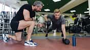 Mann trainiert mit einem Fitnesstrainer Ruderzüge im Stütz mit Kurzhanteln-