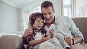 Vater und Sohn sitzen auf dem Sofa und amüsieren sich mit einem Smartphone