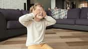 Ein Kind hält sich im Wohnzimmer die Augen zu, die restliche Familie versteckt sich hinter dem Sofa