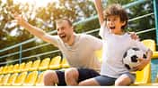 Vater und Sohn sitzen auf einer Fußballtribüne und jubeln
