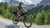 Man bikepacking, he cycles through the mountains and pine tree forests