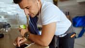 Junger Mann tippt mit Apfel und Sportkleidung auf sein Smartphone