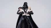 Darth Vader hält zwei übergroße Legofiguren von Leia und Luke im Arm