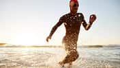 Mann rennt in Neoprenanzug und Schwimmbrille durchs Wasser