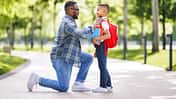 Ein Vater kniet vor seinem Sohn und macht ihn fertig für die Schule