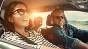 Frau und Mann sitzen gutgelaunt im Auto, auf der Rückbank sieht man ein fröhliches Kind.