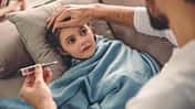 Ein Vater misst bei seiner kleinen Tochter Fieber mit Hilfe eines Thermometers