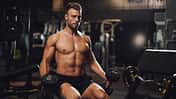 Determined young man lifting up dumbbells in the gym