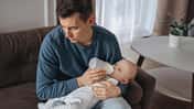Ein Vater gibt seinem Baby das Fläschchen und schaut deprimiert zur Seite
