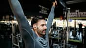 Young sportsman stretching back muscles while listening music in gym