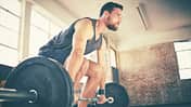 Full length of confident man dead lifting barbell in gym