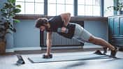 Mann macht einseitige Plank mit Hanteltraining im Home-Gym.