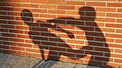 Schattenspiel: Man sieht zwei prügelnde Schulkinder auf einer Ziegelsteinwand