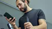 Ein Mann ist an einem Sportgerät im Fitnessstudio und schaut auf sein Handy
