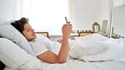 Ein Mann liegt im Bett und schaut auf sein Smartphone